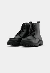 Černé kožené kotníkové boty s tkaničkami a bočním zipem, s robustní podrážkou s výrazným vzorkem a minimalistickým designem.