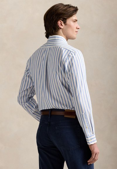 Majica z dolgimi rokavi z modro-belimi črtami, bombažno blago, gumbi na manšetah, ovratnik, v kombinaciji s temnimi denim kavbojkami in rjavim pasom.