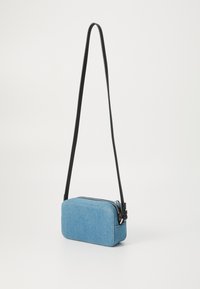 Blue denim crossbody bag with a rectangular shape, zip closure, and black adjustable strap. Features stitched detailing on the fabric.