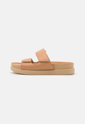 Sandale slide beige avec deux larges brides réglables et une semelle plate, vue de côté sur un fond uni.