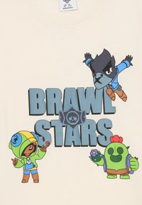 Svetlo béžové tričko s tromi kreslenými postavičkami a textom "BRAWL STARS" v tučných modrých písmenách. Postavičky majú rôzne farby a dizajny.