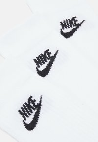 Weiße Baumwoll-Crew-Socken mit einem schwarzen, gestickten Nike-Logo und einem Swoosh-Design am oberen Ende. Weicher Stoff mit geripptem Bündchen.