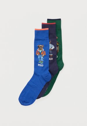 Trois chaussettes colorées en bleu, marine et vert, chacune présentant un ours portant des tenues décontractées et le mot « POLO » sous le motif de l'ours.