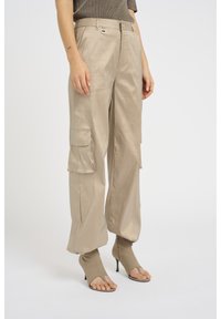 Beige cargo-housut, joissa on sileä pinta, sivutaskut ja rento leikkaus. Yhdistetty avonaisiin kärkiin ja korkeat nilkkasaappaat samaan sävyyn.