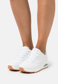White athletic shoes with a smooth surface, mesh accents, and a gum rubber sole. Features a lace-up design and visible air cushioning.