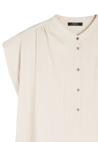 Jasno beżowa koszula zapinana na guziki, wykonana z miękkiego materiału. Posiada wyraźny kołnierz, krótki rękaw oraz subtelne plisowania na ramionach.