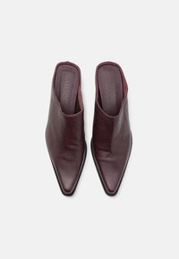 Mules de cuero burdeos con diseño de punta, texturizados suaves y lados minimalistas. Logo estampado en las plantillas.