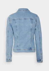 La chaqueta de mezclilla azul claro presenta un cuello con solapa, mangas largas y un diseño ajustado con costuras visibles y un yugo en la parte posterior.