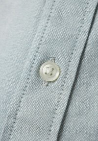Lichtblauwe stof met een fijne textuur, met een grote doorzichtige knop met een ontwerp met vier gaten, en zichtbare stiksels langs de naad.
