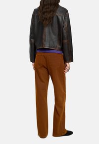Brązowa skórzana kurtka w kroju cropped na purpurowym swetrze ribbed, zestawiona z brązowymi szerokimi spodniami i czarnymi butami, widok z tyłu.