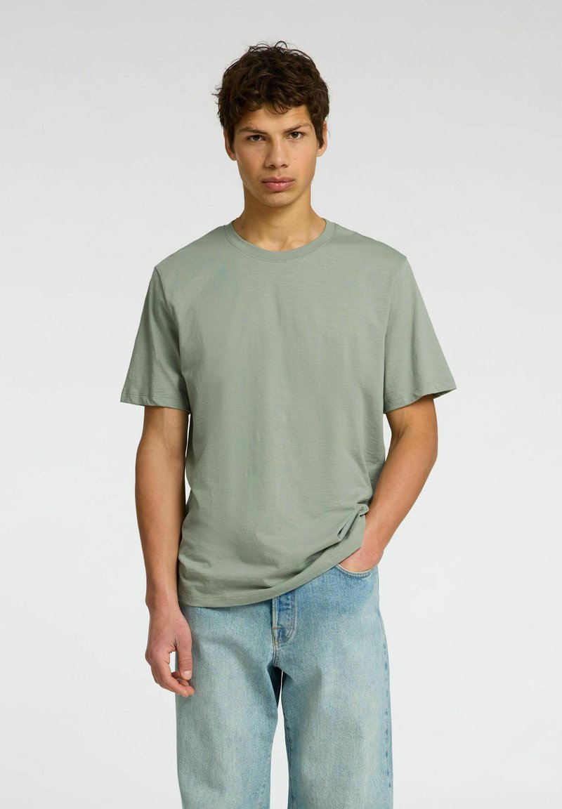Camiseta de algodón verde claro con cuello redondo y mangas cortas; combinada con jeans azul claro; textura suave, corte relajado.