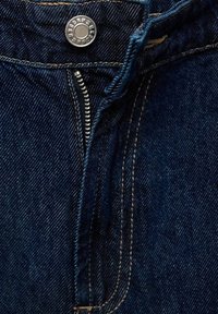 Tessuto di denim blu scuro con chiusura frontale a cerniera e bottone in metallo. Presenta cuciture fini e una texture robusta.