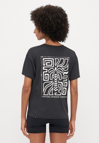 T-shirt nero a maniche corte con un design grafico bianco caratterizzato da motivi astratti ed elementi di palma sul retro. Texture del tessuto liscia.