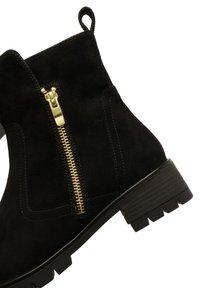 Black suede ankle boot with chunky heel, rugged sole, side gold zipper, and pull tab at the back.