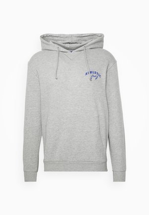 Grå hættetrøje med frontlomme og blå grafisk detalje; slidte blå denimshorts med opklemte kanter; hvide høje sneakers, stående på en træterrasse.