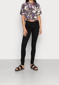 Top gráfico recortado con diseño floral en púrpura, rosa y beige; jeans ajustados negros; sandalias de plataforma negras con correas acolchadas.