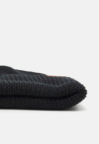 Maglione nero a maglia con una texture a coste, dotato di orlo piegato e di una piccola etichetta marrone decorativa sul lato.