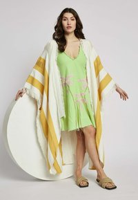Kevyt kimono, jossa on keltaisia ja valkoisia raitoja, fringed-reunat, käytetty vihreän mekon päällä, jossa on vaaleanpunaista kukka-ompelua.
