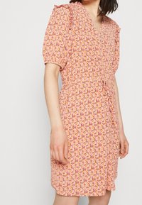 Donna che indossa un vestito corto a maniche a palloncino, lungo fino al ginocchio, con un motivo floreale in arancione, rosa e bianco e scollo a V.