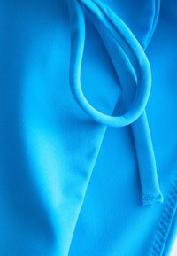 Tissu bleu vif avec un cordon bouclé et des coutures visibles, probablement une partie d'un vêtement ou accessoire.