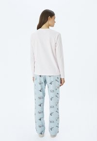 Lichtroze langarmtop en blauwe pyjamabroek met cartoonpatronen, met illustraties van skiërs en sneeuwvlokken. Zachte stof.