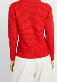 Czerwony sweter dziany z teksturowanym, prążkowanym wzorem, z długimi rękawami i dopasowanym mankietem, zaprojektowany z wysokim kołnierzem dla dodatkowego ciepła.