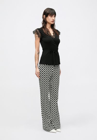 Czarny top z krótkim rękawem ozdobiony koronką, zawiązany w talii; w połączeniu z białymi spodniami o szerokich nogawkach i geometrycznym wzorze oraz białymi, spiczastymi butami.