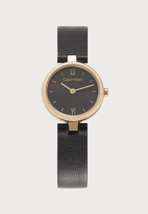 Reloj Calvin Klein redondo negro con bisel dorado, marcadores de hora dorados, dos agujas doradas y correa de cuero negra.