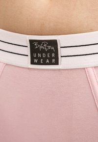 Gros plan sur un sous-vêtement rose clair avec une ceinture blanche portant une étiquette noire indiquant « Björn Borg UNDERWEAR ».