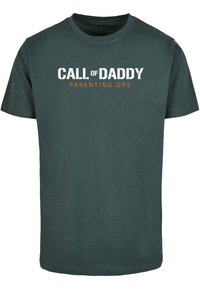 Camiseta de algodón verde oscuro de manga corta. En la parte frontal presenta "LLAMADA de PAPÁ" en blanco y "OPERACIONES DE PARENTALIDAD" en naranja. Cuello redondo.