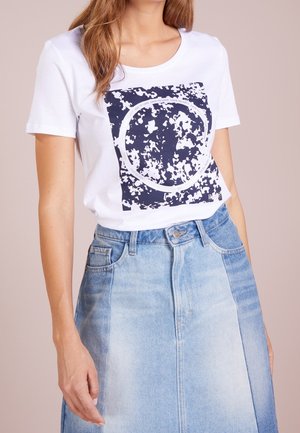 Weißes Baumwoll-T-Shirt mit einem maritimen grafischen Design, das ein kreisförmiges Muster zeigt. Kombiniert mit einem hellblauen Denim-Rock, der einen klassischen Schnitt hat.