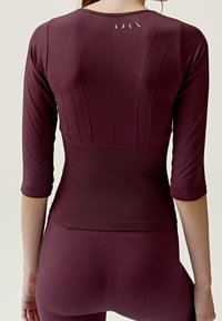 Burgundy träningströja med trekvartslånga ärmar, ribbat mönster, horisontella och vertikala paneler, samt diskreta logotypdetaljer på baksidan.