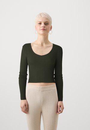 Long-sleeve, dark green ribbed top with a V-neck design, paired with light beige, ribbed, high-waisted pants. Fabric appears soft and stretchy.