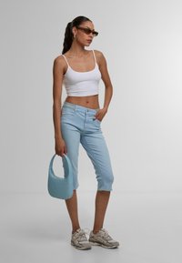 Lyseblå, croppede jeans med en afslappet pasform, parret med en hvid, tætsiddende tanktop. Holder en struktureret lyseblå håndtaske og bærer solbriller.