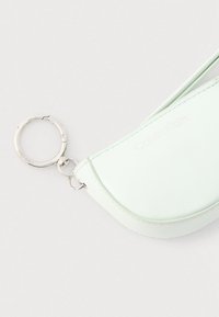Φωτεινή μέντα πράσινη θήκη Calvin Klein με ασημένιο κρίκο για κλειδιά πάνω σε ανοιχτό γκρι φόντο.