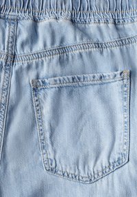 Helle blaue Jeans im Rücken mit einem elastischen Bund und einer quadratischen Eintrittstasche mit kontrastierenden Nähten. Glatte, leicht ausgewaschene Textur.