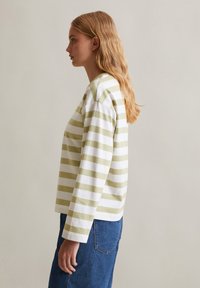 Langsleeve gestreepte shirt in groen en wit. Heeft een ronde halslijn en een ontspannen pasvorm, gemaakt van zachte katoen. Gecombineerd met blauwe jeans.