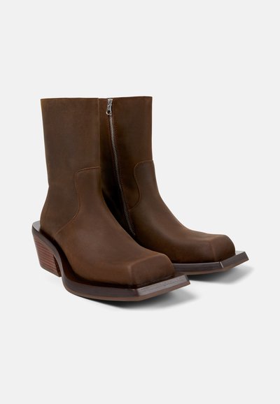 Bottines en cuir marron avec une fermeture à glissière sur le côté, bout carré et talon épais. Texture lisse avec des accents boisés sur la base.