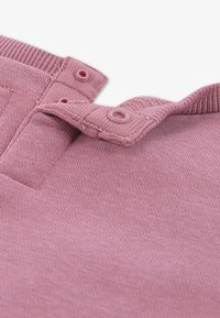 Maglione lavorato a maglia rosa con una finitura testurizzata, caratterizzato da un colletto a coste e due bottoni a pressione per la chiusura all'altezza del collo.