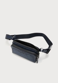 Τσάντα μέσης Michael Kors σε ναυτικό μπλε με διπλές θήκες με φερμουάρ και ρυθμιζόμενο λουρί σε λευκό φόντο.