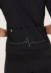 Svart atletisk topp med ett hjärtslagsmönster i vitt på baksidan, med en bakficka och en figurnära design. Strukturerad tyg med elastisk nederkant.