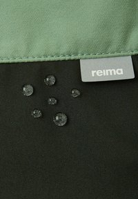 Mustaa kangasta, jonka pinnalla on vesipisaroita, täydentää vihreä ylureuna ja harmaa etiketissä lukee "reima."
