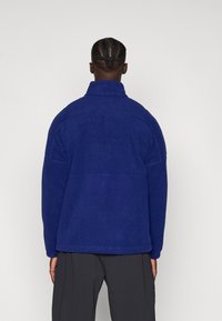 Fleece jack in diepblauw met een hoge kraag, gestructureerd oppervlak en gestikte accenten. Beschikt over een relaxte pasvorm en lange mouwen.