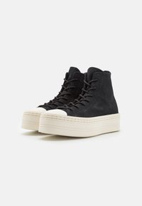 Black suede high-top sneakers with a white rubber toe cap and a thick cream platform sole, featuring rounded laces and a smooth texture.