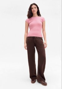 Top corto de manga corta a rayas rosas combinado con pantalones anchos de pierna oscura. El material parece suave con una textura lisa. Unos zapatos marrones completan el look.