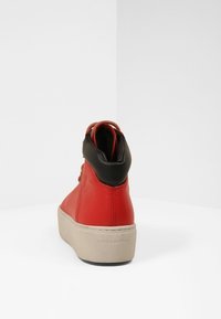 Czerwone skórzane sneakersy za kostkę z czarnymi akcentami, z teksturowaną powierzchnią i beżową podeszwą platformową. Na pięcie widoczna nazwa marki "VAGABOND".