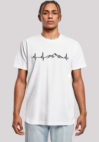 White cotton t-shirt featuring a black heartbeat line graphic with mountain peaks, round neck, and short sleeves. Smooth texture.
