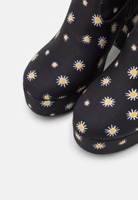 Czarne botki za kostkę z kwiatowym wzorem białych stokrotek o żółtych środkach. Charakteryzują się gładkim wykończeniem z tkaniny oraz zaokrąglonym noskiem.