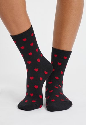 Calcetines negros con un patrón de pequeños corazones rojos. La textura parece suave, con un diseño de longitud estándar en estilo crew.
