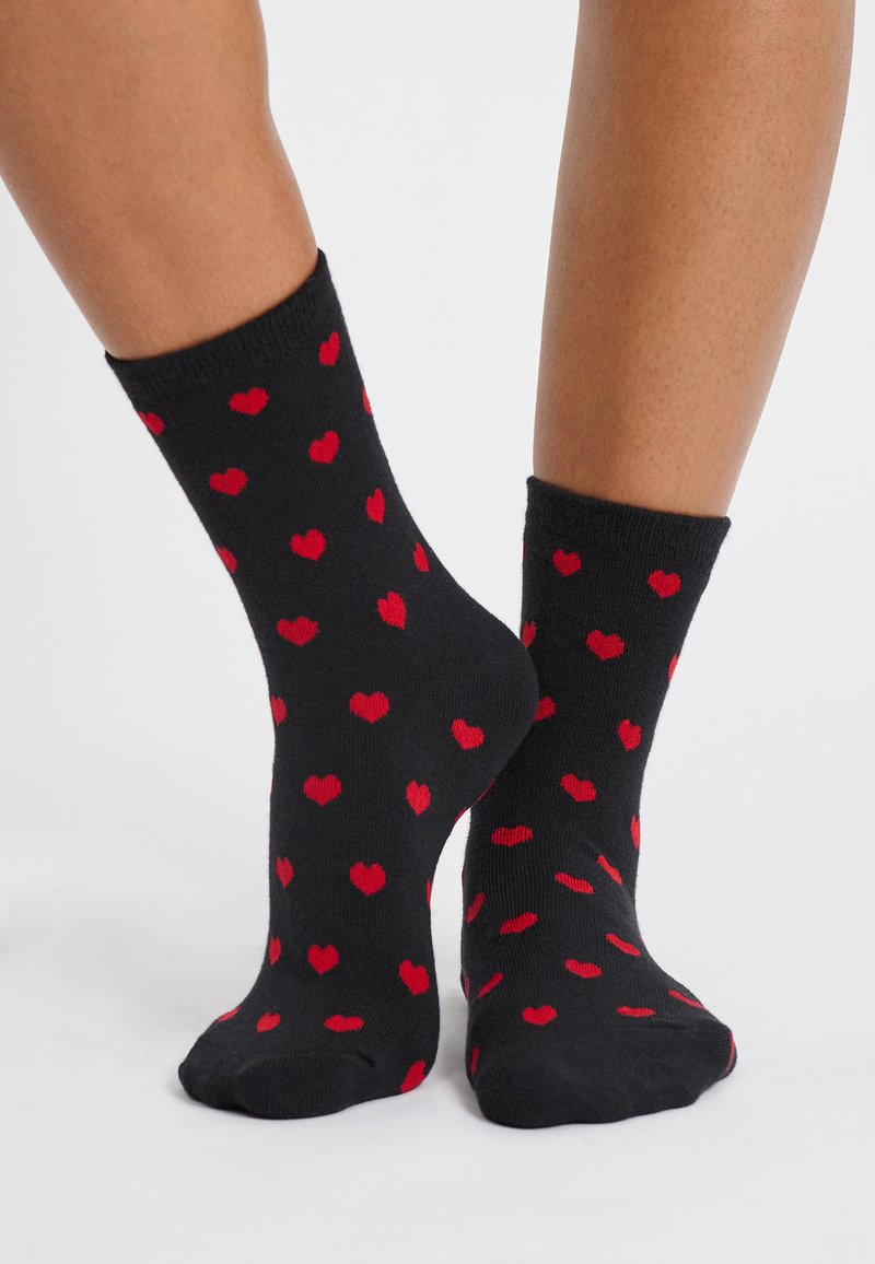 Calzini neri con un motivo di piccoli cuori rossi. La texture appare liscia, con un design di lunghezza normale.